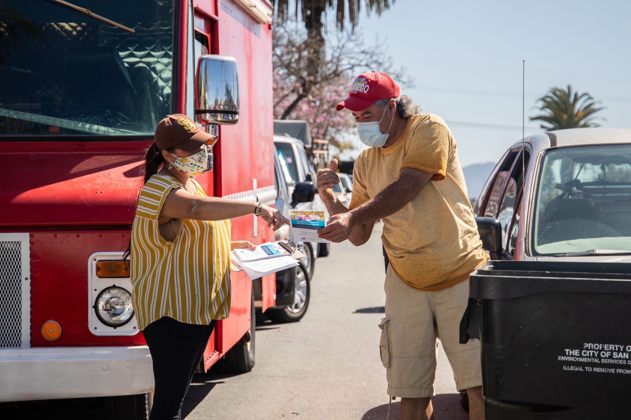 A community volunteer hands a Logan Heights resident a flyer with information on scheduling a COVID-19 vaccine appointment in March 2021. / Photo by Adriana Heldiz