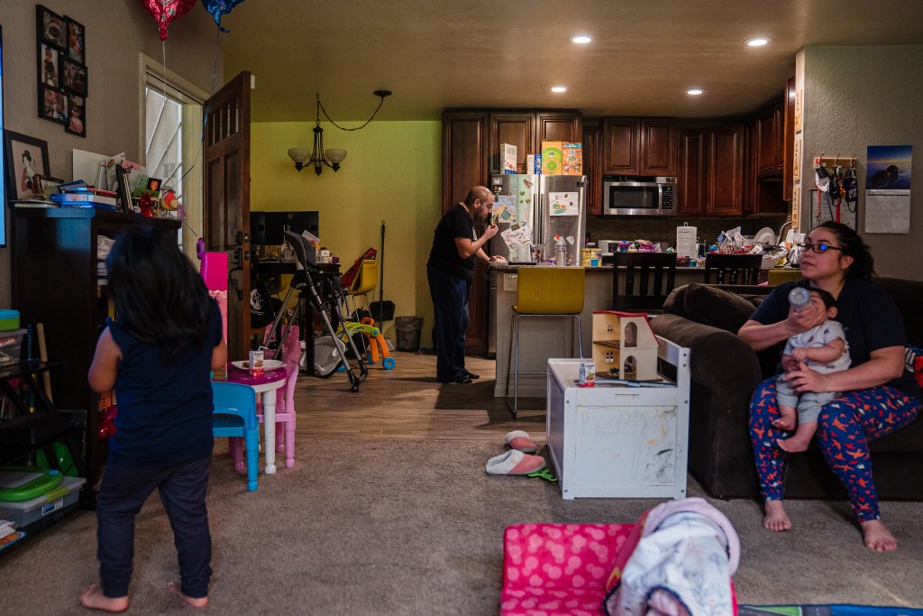 Sophia Rodriguez's husband Dan works on his computer through lunch while Sophia gives a bottle to their 10-month-old son and their daughter watches television at home in Chula Vista on March 8, 2022.