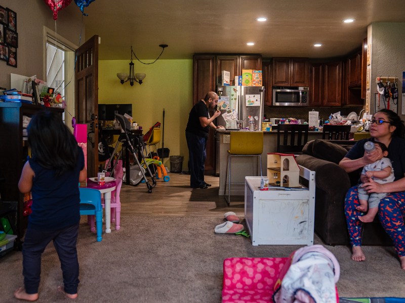 Sophia Rodriguez's husband Dan works on his computer through lunch while Sophia gives a bottle to their 10-month-old son and their daughter watches television at home in Chula Vista on March 8, 2022.