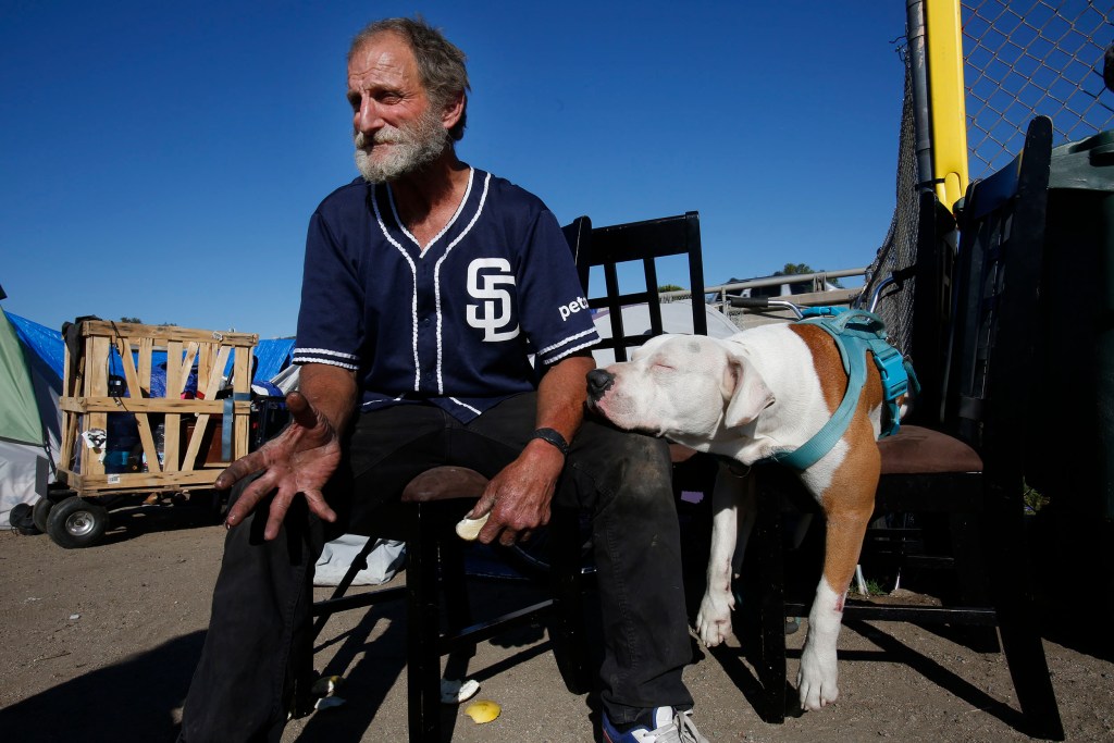 Gerald (Gerry) Kostiha eats a grapefruit while sitting on a chair outside his tent Tuesday, March 8, 2022 in El Cajon, CA.
