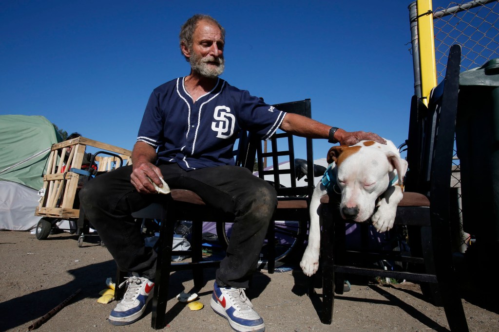 Gerald (Gerry) Kostiha eats a grapefruit while sitting on a chair outside his tent Tuesday, March 8, 2022 in El Cajon, CA.