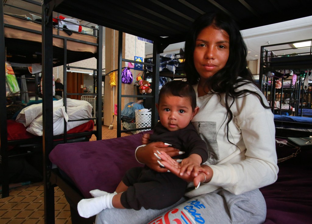Kassandra Martinez, 19, and her son Adrian Martinez, 6 months, share a bunk in the family shelter area of Golden Hall in the downtown San Diego Civic Center Concourse on April 8, 2022. Her two female cousins and their children are also at the shelter. / Photo by Peggy Peattie for Voice of San Diego