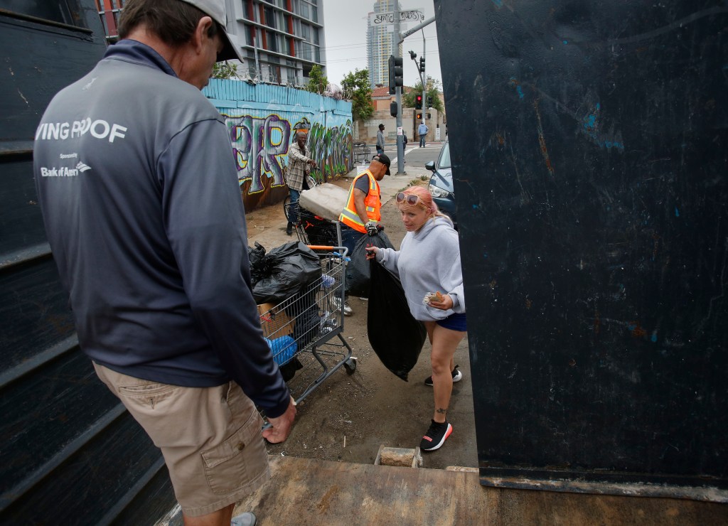 Victoria Bell, 34, right, brings a shopping cart full of trash-filled bags to Brian Trotier, left, of the Triangle Project. Bell is a regular participant of the project, and collects $2 per bag of trash. / Photo by Peggy Peattie for Voice of San Diego
