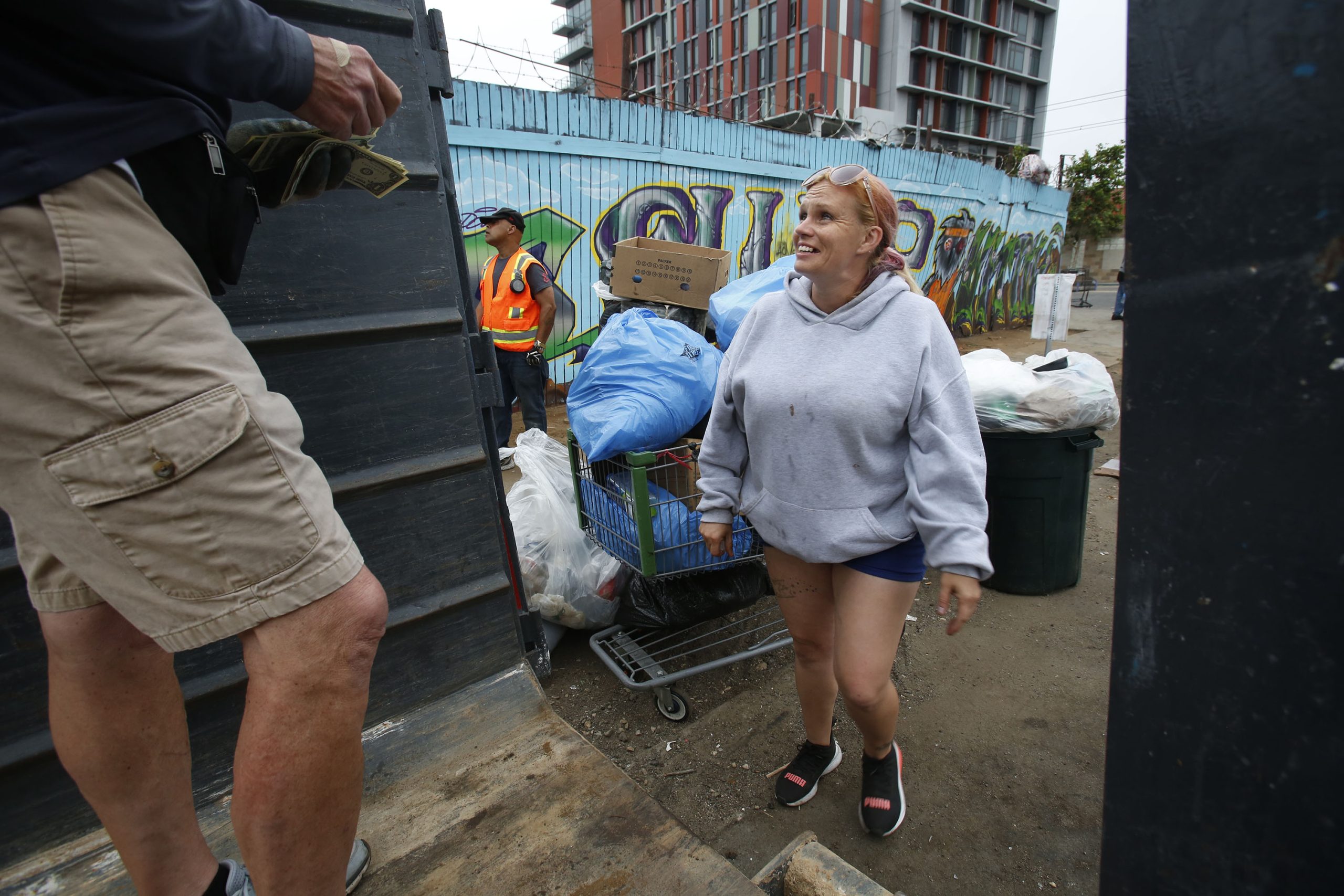 Victoria Bell, 34, right, brings a shopping cart full of trash-filled bags to Brian Trotier, left, of the Triangle Project. Bell is a regular participant of the project, and collects $2 per bag of trash. / Photo by Peggy Peattie for Voice of San Diego