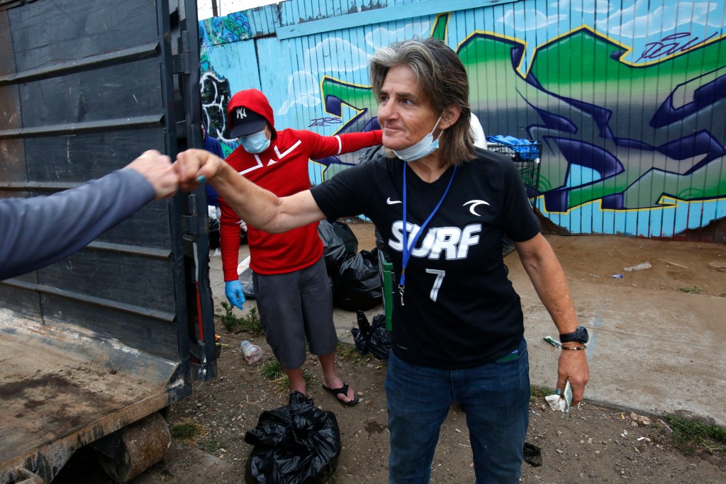 Kathy Shely, 55, right, gives a fist bump to Triangle Project co-founder Brian Trotier after receiving cash for the bags of trash she'd brought to the dumpster on Monday, June 13, 2022. / Photo by Peggy Peattie for Voice of San Diego
