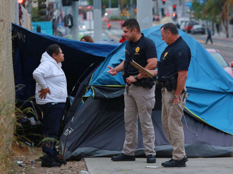 Members of the Police Department's Homeless Outreach Team talk with a woman living in a tent on Commercial Street just after sunrise on Monday, June 13, 2022. / Photo by Peggy Peattie for Voice of San Diego