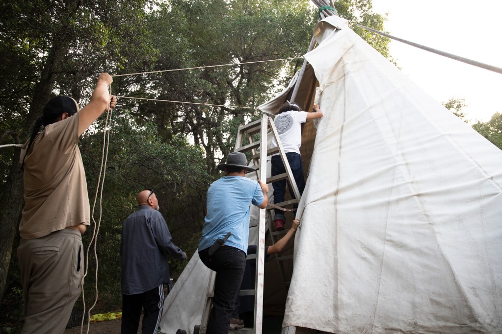 Men use rope to secure the canvas to the frame. / Photo by Jakob McWhinney