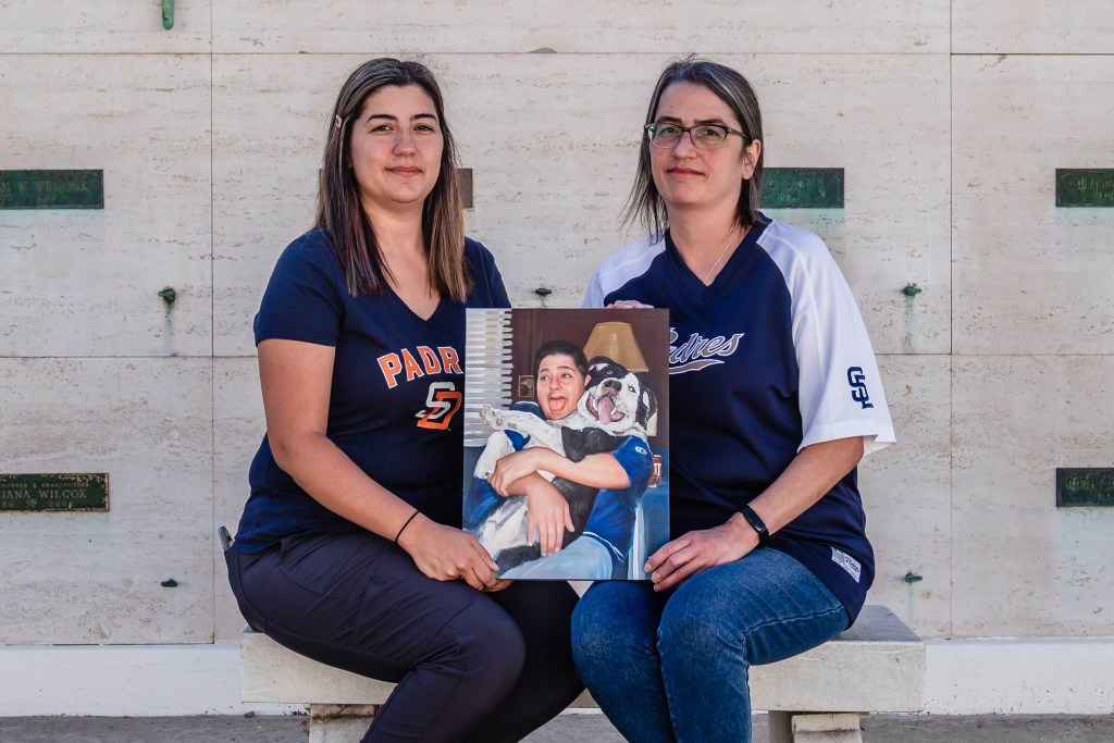 Ashely Jepsen (left) and Stephanie Campbell (right) hold a painting of their brother Dale Campbell II at Eternal Hills Mortuary and Crematory on Nov. 22, 2022, who passed away from complications from Covid-19.