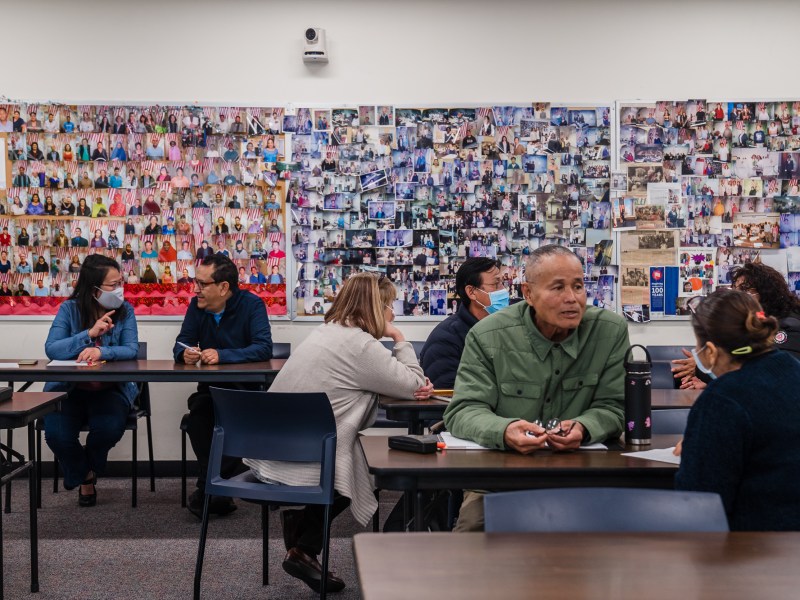Students work in pairs in front of a wall of photographs of former students who have successfully become citizens during a a March 20, 2023 citizenship class at the San Diego College of Continuing Education’s Mid-City Campus. / Photo by Ariana Drehsler