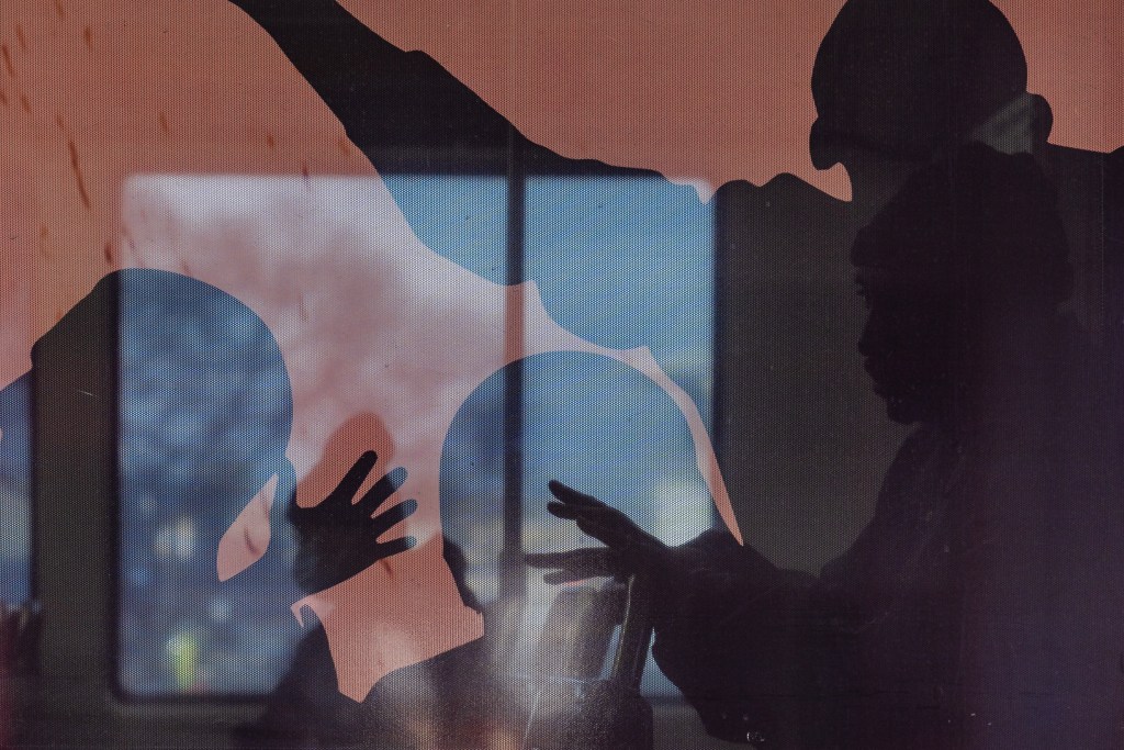 A man can be seen sitting in the trolley through a silhouetted pictured window at 12th and Imperial Avenue trolley station on May 1, 2023.