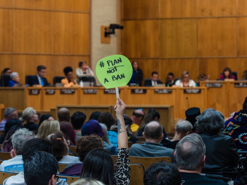 A woman holds as sign that reads "Plan Not a Ban" in the City Council Chambers opposing the homeless camping ban in downtown on June 13, 2023.