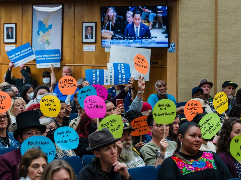 Mayor Todd Gloria speaks in City Council Chambers in downtown while people hold signs opposing the homeless camping ban on June 13, 2023.
