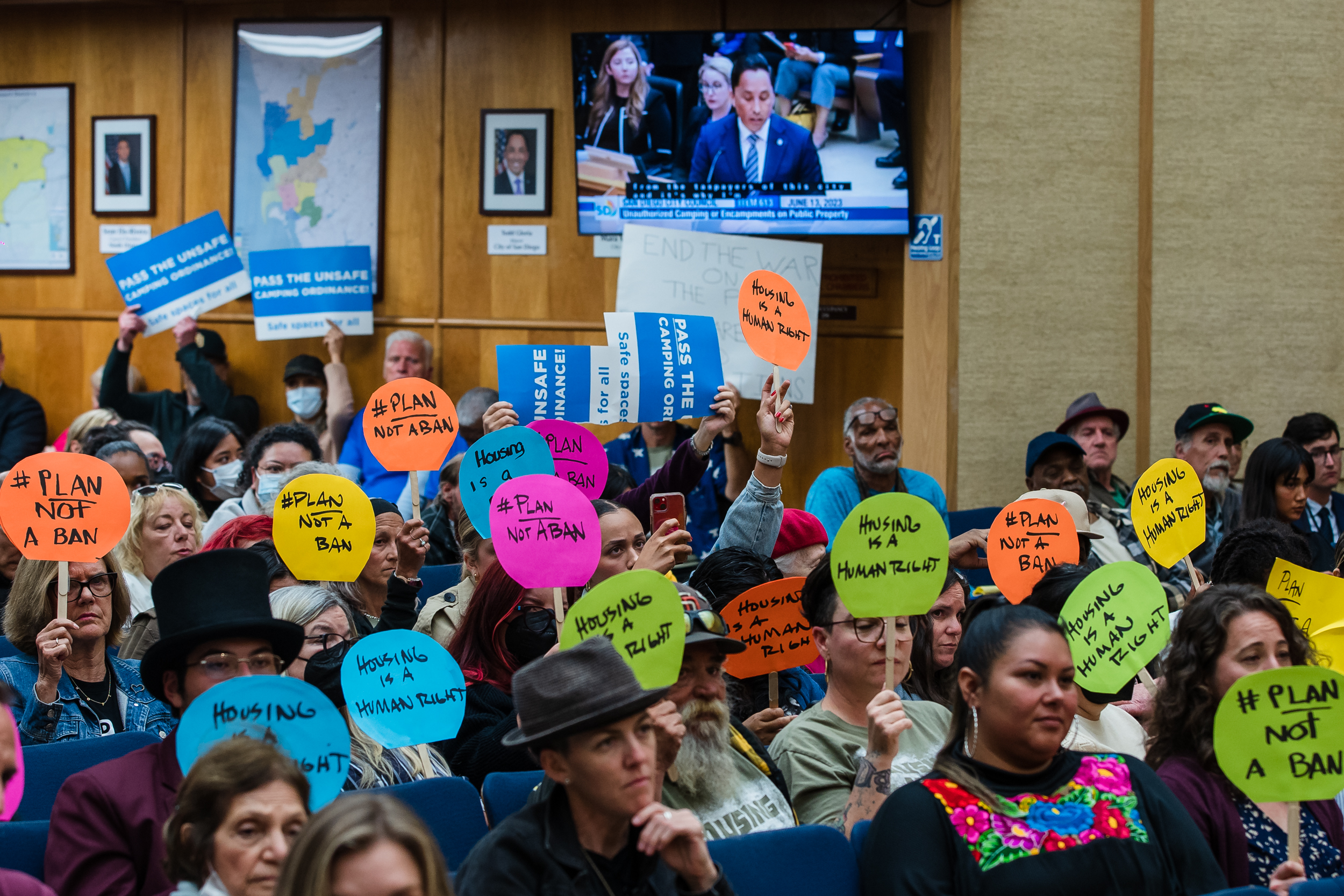 Mayor Todd Gloria speaks in City Council Chambers in downtown while people hold signs opposing the homeless camping ban on June 13, 2023.