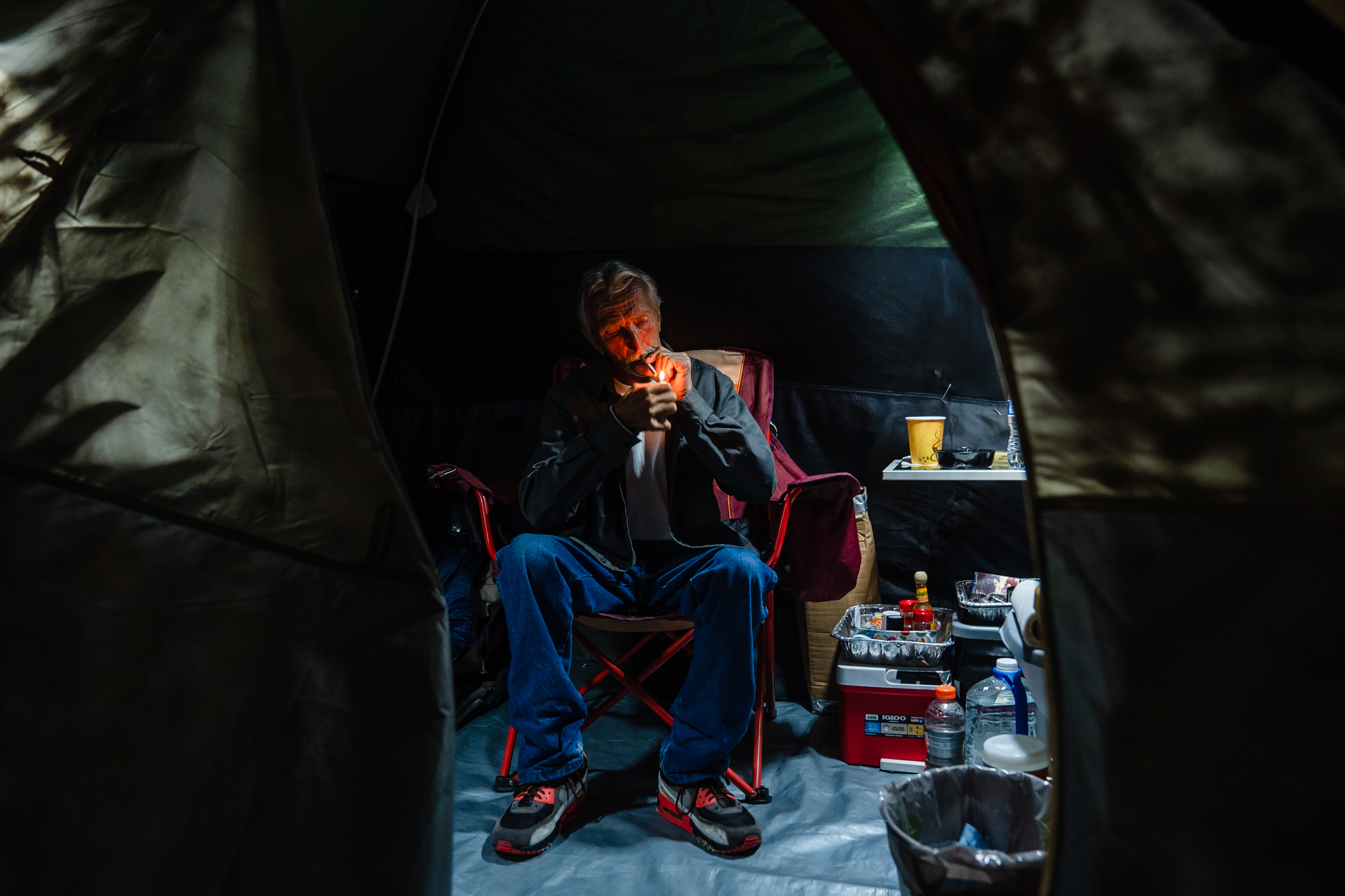 TW, 68 years old from Maine lights up a cigarette in his tent at a homeless encampment on Commercial Street in downtown on March 30, 2023. TW says he enjoys cooking and keeping his tent clean and organized. He came to San Diego last June from Arizona. TW stayed at Father Joe's before staying at an encampment. / Photo by Ariana Drehsler