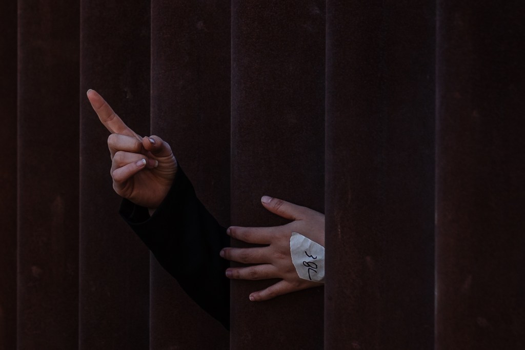 A young woman's hands through the border wall in San Ysidro on Sept. 12, 2023.