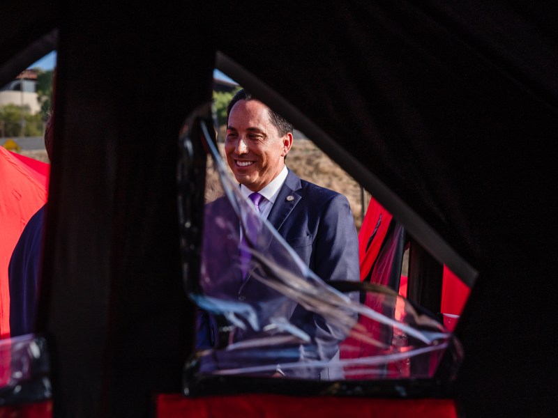San Diego Mayor Todd Gloria through an opening of a tent at at the Lot Safe Sleeping site on the edge of Balboa Park and near the Naval Medical Center on Oct. 20, 2023.