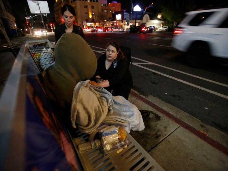 Amanda Giovanetti, left, and Laura Chechel, kneeling, gently wake Edward, on a bus bench on Washington Street in Hillcrest on July 2, 2023. Edward asked that Voice of San Diego not use his last name.