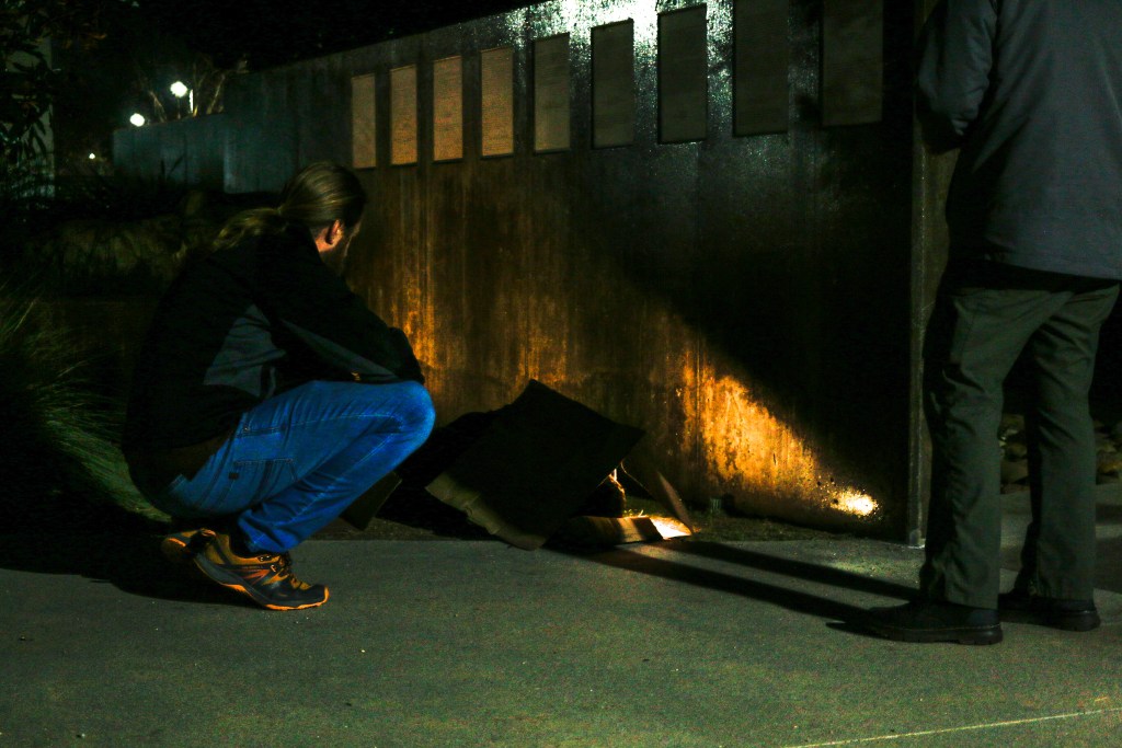 A volunteer with the Regional Taskforce on Homelessness conducting the annual point-in-time count speaks to a man sleeping on a sidewalk in downtown Vista on Thursday, Jan. 25, 2024. / Photo by Tigist Layne