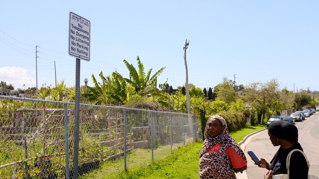 Fatima Abdelrahman, a Sudanese refugee, and Sahar Abdalla, outside the New Roots Community Farm. A sign next to the garden fence says, "property of the city of San Diego," but the ownership of the land is being disputed. / Photo by MacKenzie Elmer