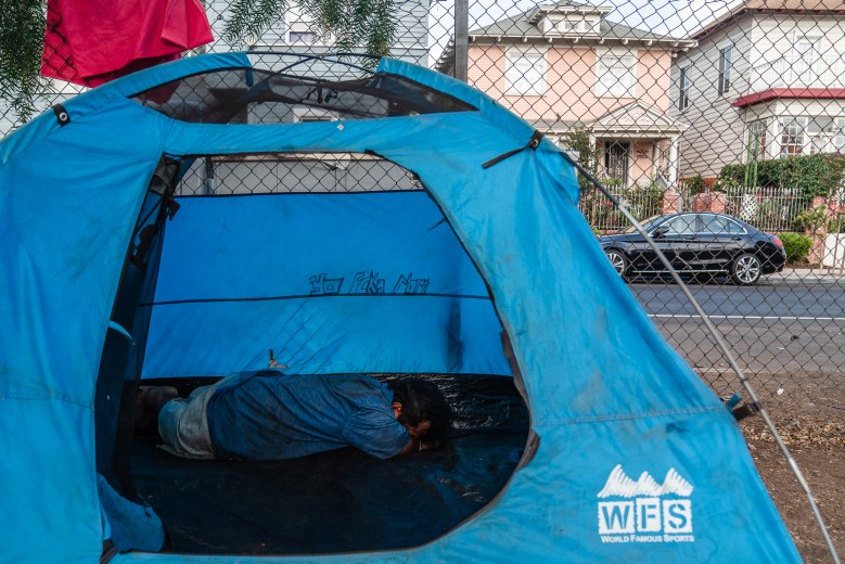 A man rests in a tent at a homeless encampment next to Interstate 5 North ramp near downtown San Diego on July 15, 2025. / Ariana Drehsler for Voice of San Diego