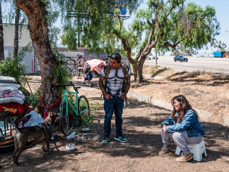 Alyssa her boyfriend Jonathan and their dog Diesel at a homeless encampment next to the Interstate 5 North ramp on July 16, 2025, outside of downtown San Diego. / Ariana Drehsler for Voice of San Diego